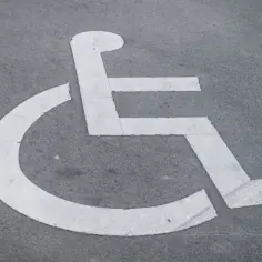 Symbol wózka inwalidzkiego na drodze, przypominający o potrzebie wypełnienia wniosku o wydanie karty parkingowej.