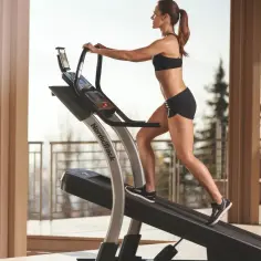 Kobieta ćwiczy na bieżni NordicTrack na tarasie z widokiem na drzewa.