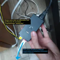 Ręka trzyma czarny adapter sieciowy. Żółty kabel od odbiornika jest podłączony do adaptera. Biały kabel sieciowy, który chcesz podłączyć do komputera, jest gotowy.