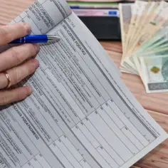Ręka z długopisem nad deklaracją podatkową, obok stos banknotów. Czas na rozliczenie, kiedy zwrot podatku jest na wyciągnięcie ręki.