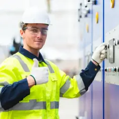 Elektryk w kamizelce odblaskowej przy panelu sterowania. Pewny siebie pracownik, jeden z wielu dostawców prądu w Polsce, dba o bezpieczeństwo.