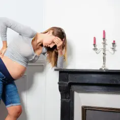 Ciężarna kobieta z ręką na plecach i czole, odczuwająca ból jajnika w ciąży.