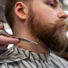 Stylista przycina brodę mężczyzny, pokazując, jak zapuścić brodę przy słabym zaroście.