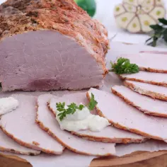 Soczysta szynka pieczona w rękawie, pokrojona w plastry, z chrzanem i natką pietruszki. Idealna na wielkanocny stół.