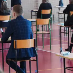 Uczniowie siedzą w ławkach podczas egzaminu, przygotowując się do maturalnych wymagań z biologii.