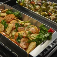 Pyszne warzywa, takie jak marchewka i ziemniaki, pieczone w metalowym koszu do grilowania, z dodatkiem ziół i jarmużu.