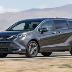 Szary minivan Toyota Sienna pędzi po pustynnej drodze, z górzystym krajobrazem w tle.