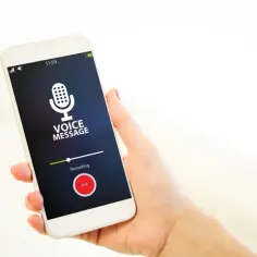 Dłoń trzyma smartfon z ekranem pokazującym interfejs nagrywania wiadomości głosowej. Widoczny jest przycisk "Stop" i napis "Recording", co ilustruje, jak włączyć dyktafon w telefonie.