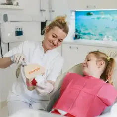Dentystka pokazuje model szczęki dziecku w gabinecie stomatologicznym.