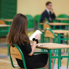 Dziewczyna w czarnej sukience trzyma kartkę, czekając na wyniki egzaminów zawodowych.
