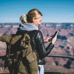 Kobieta z plecakiem sprawdza telefon, być może co to jest roaming danych, na tle Wielkiego Kanionu.