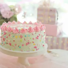 Jasnozielony tort z różową posypką i kremem, obok prezenty. Zastanawiasz się, ile kosztują torty na przyjęcie?