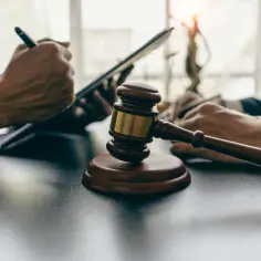 Młotek sędziowski na stole, obok dłoni prawników pracujących z dokumentami i tabletem.