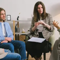 Grupa osób uczestniczy w sesji psychoterapii systemowej. Terapeuta prowadzi rozmowę, słuchając uważnie uczestników.
