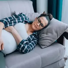 Kobieta w ciąży leży na kanapie, cierpiąc z powodu objawów listeriozy.