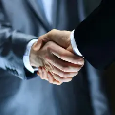 Dwaj mężczyźni w garniturach ściskają sobie dłonie, symbolizując udane partnerstwo i zawarcie umowy.