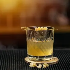 Orzeźwiający drink Ballantines z colą, ozdobiony kandyzowanym imbirem, na drewnianym podkładzie.