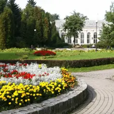 Kolorowe rabaty kwiatowe w parku, z alejką i budynkiem w tle. Idealne miejsce na spacer po cieplicach.