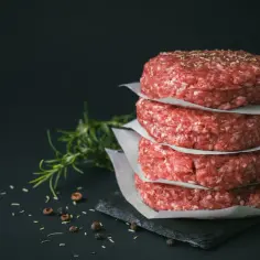 Stos surowych kotletów na burgery, idealne mięso na mielone, z gałązką rozmarynu i pieprzem w tle.
