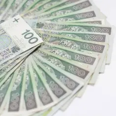 Ułożone wachlarzowo banknoty 100 zł, symbolizujące świadczenie urlopowe, gotowe na wymarzone wakacje.