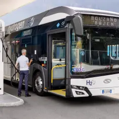 Mężczyzna tankuje autobus elektryczny na stacji wodorowej. Pojazd z napisem "Hydrogen H2" jest gotowy do dalszej podróży.