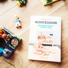 Książka "Montessori. Wychowanie dziecka w wieku 0-6 lat" obok klocków i figurek, inspiruje do nauki przez zabawę.