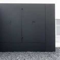 Nowoczesna zabudowa skrzynki elektrycznej w ogrodzeniu, z dyskretnymi symbolami.