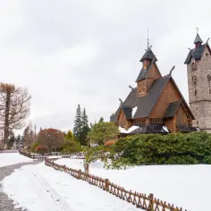 Drewniany kościółek i kamienna wieża zegarowa w zimowej scenerii. To urokliwe miasto u podnóża Śnieżki, gdzie śnieg otula ścieżki i drzewa.