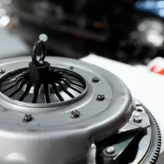 Element sprzęgła, gotowy do wymiany. W tle widać fragment samochodu, sugerujący prace mechaniczne.