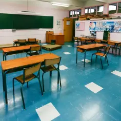 Pusta klasa z niebieską podłogą i drewnianymi ławkami. Nauczyciel zastanawia się, ile wcześniej trzeba zapowiedzieć sprawdzian.