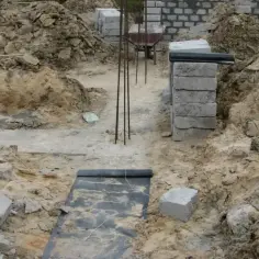 Wykonano wykopy pod fundamenty. Widać zbrojenie, bloczki betonowe i ziemię.