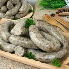 Pyszna, domowa biała kaszanka na drewnianej desce, ozdobiona natką pietruszki. Obok widoczne drewniane sztućce i ziarna pieprzu.