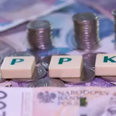 Pieniądze na stole, litery PPK i stosy monet. Zastanawiasz się, jak wypłacić pieniądze z PPK?