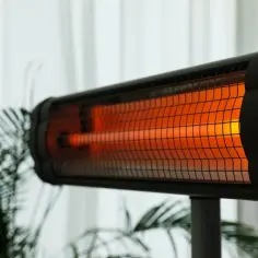 Grzejnik na podczerwień z rozżarzonym elementem grzewczym, na tle roślin i zasłon.