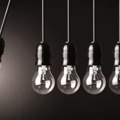 Wisząca żarówka energooszczędna, symbolizująca pracę i moc, przekazuje energię do kolejnych, tradycyjnych żarówek.