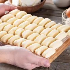 Ania gotuje pierogi leniwe. Na desce leżą rzędy gotowych do gotowania pierogów leniwych, obok jajka i twaróg.