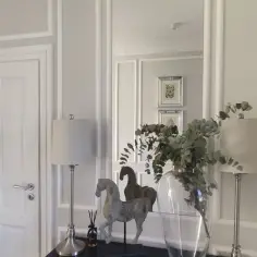 Elegancka sztukateria w przedpokoju podkreśla klasyczny styl. Dwa koniki, lampy i wazon z gałązkami dodają uroku.