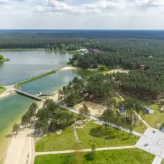 Malowniczy zalew w Janowie Lubelskim otoczony lasem, z piaszczystymi plażami, pomostami i nowoczesną architekturą.
