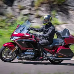 Mężczyzna w kasku jedzie lśniącym, czerwonym motocyklem Honda. To jeden z tych motocykli, które zachwycają miłośników marki.