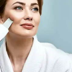 Kobieta w szlafroku wykonuje peeling kawitacyjny w domu, ciesząc się domowym spa.