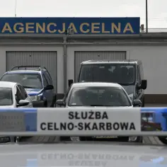 Służba celno skarbowa czuwa nad bezpieczeństwem. W tle budynek agencji celnej i zaparkowane samochody.