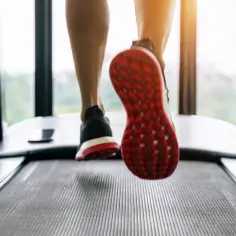 Intensywne bieganie na bieżni. Widok z dołu na nogi w sportowych butach, z czerwonymi podeszwami, w ruchu.
