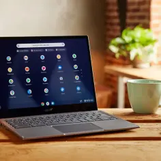 Laptop z systemem Chrome OS Flex na drewnianym stole, obok kubek i klucze.