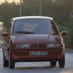 Pomarańczowy BMW E1 jedzie po drodze.