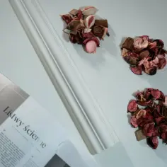 Białe listwy narozne scienne obok ozdobnych suszonych kwiatów i otwartej książki.