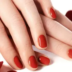 Dłonie z idealnym, czerwonym manicure. Lśniące tytanowe paznokcie, otoczone płatkami czerwonych róż, emanują elegancją i zmysłowością.
