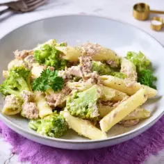 Penne z tuńczykiem i brokułami w kremowym sosie śmietanowo-serowym, udekorowane natką pietruszki.
