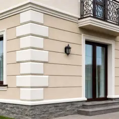 Eleganckie boniowanie podkreśla narożnik jasnego domu z brązowymi oknami i drzwiami.