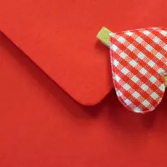 Czerwona koperta z serduszkiem w kratkę, symbolizująca wzruszający list do żony.