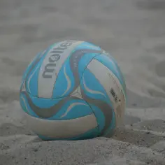 Piłka do siatkówki plażowej Molten na piasku, w kolorach białym, niebieskim i szarym.